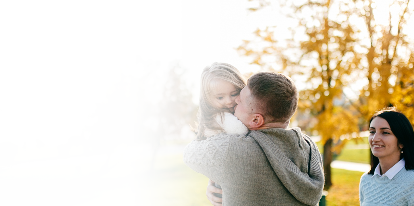Father holding young daughter in a park with autumn foliage, symbolizing family security and investment in future, relevant to Indexed Universal Life insurance.
