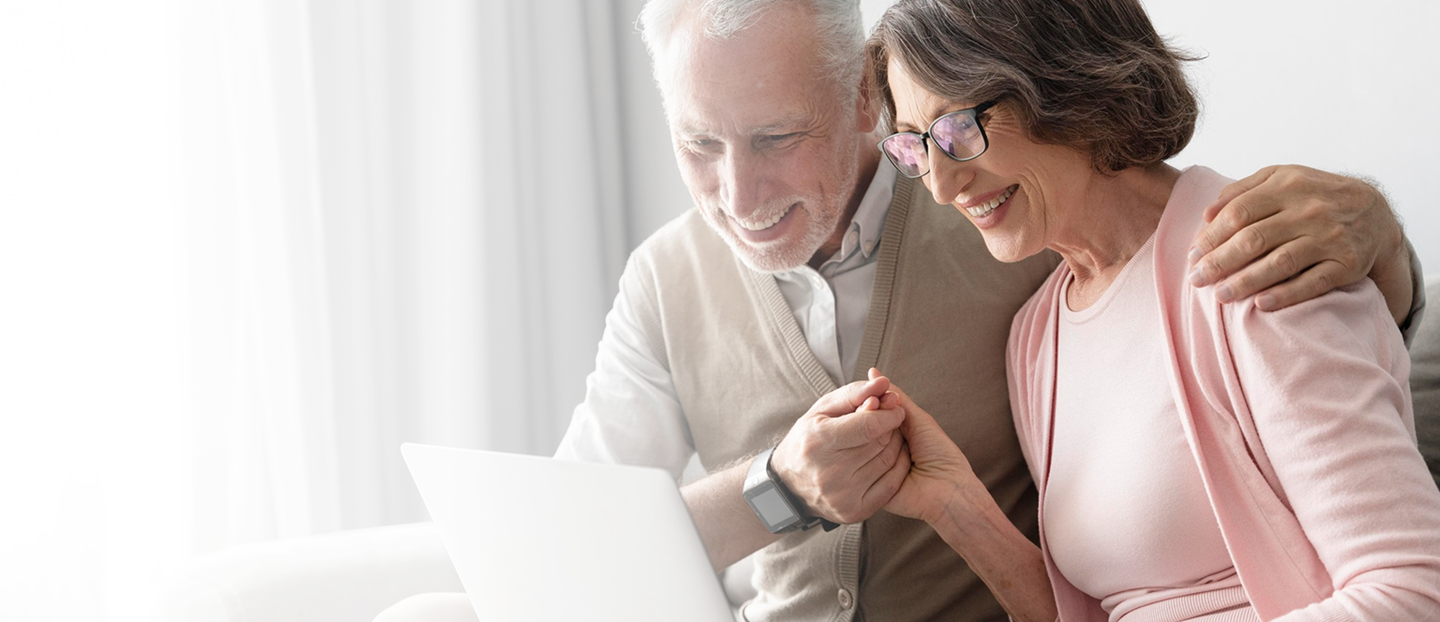 Senior couple smiling and engaging with a laptop, representing personalized senior insurance solutions and support for Medicare and retirement planning.