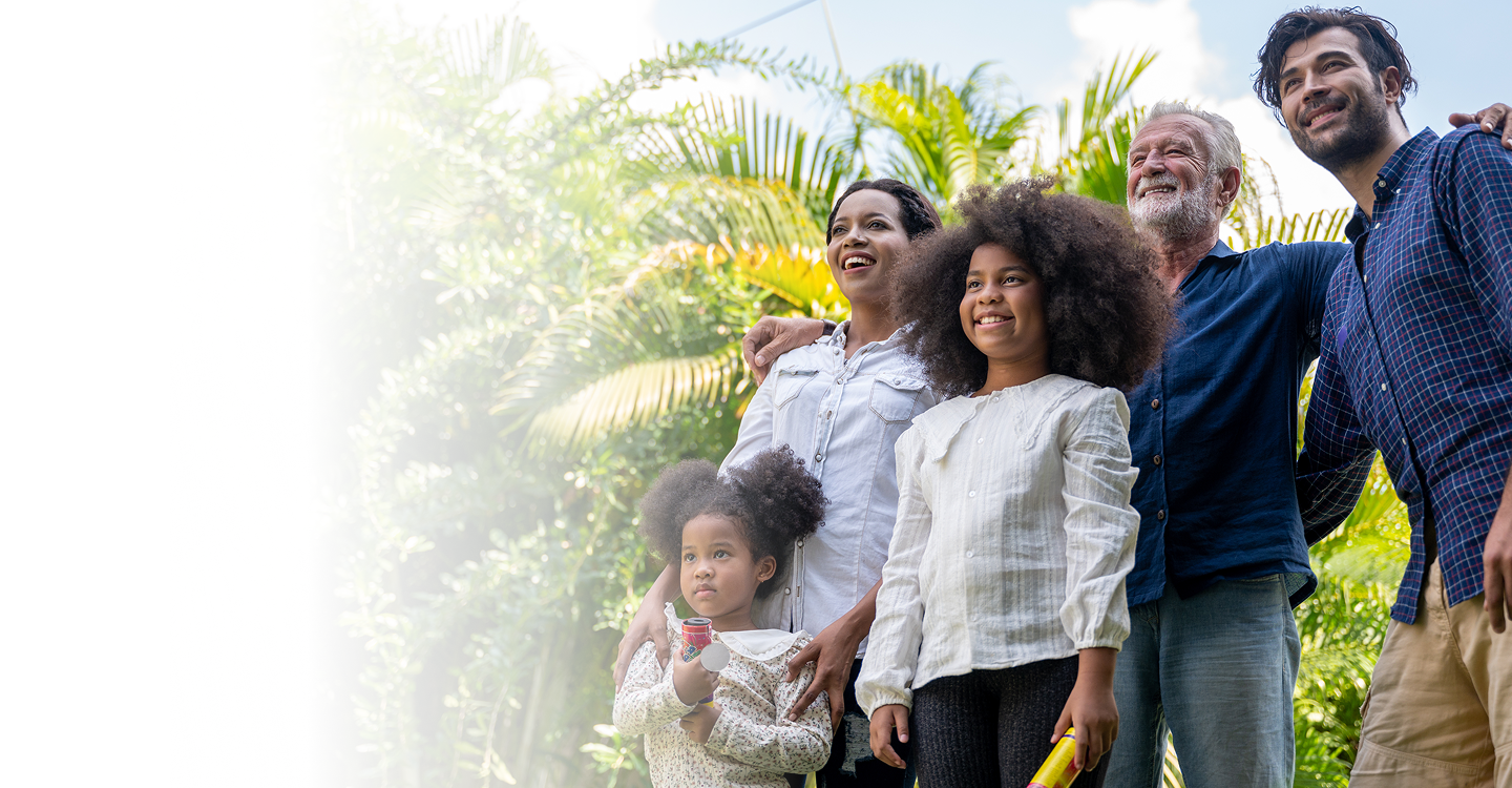 Family of five smiling together outdoors, surrounded by lush greenery, representing connection and well-being, relevant to accessible health coverage options.