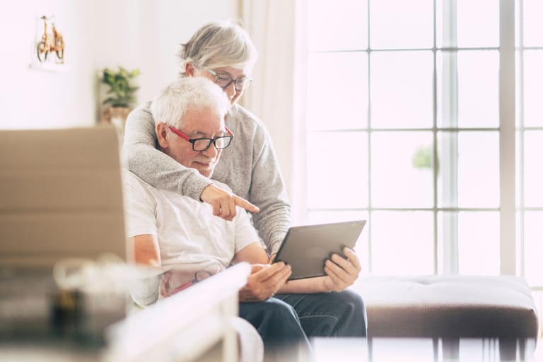 Elderly couple engaged in retirement planning, using a tablet in a bright, comfortable living room setting.