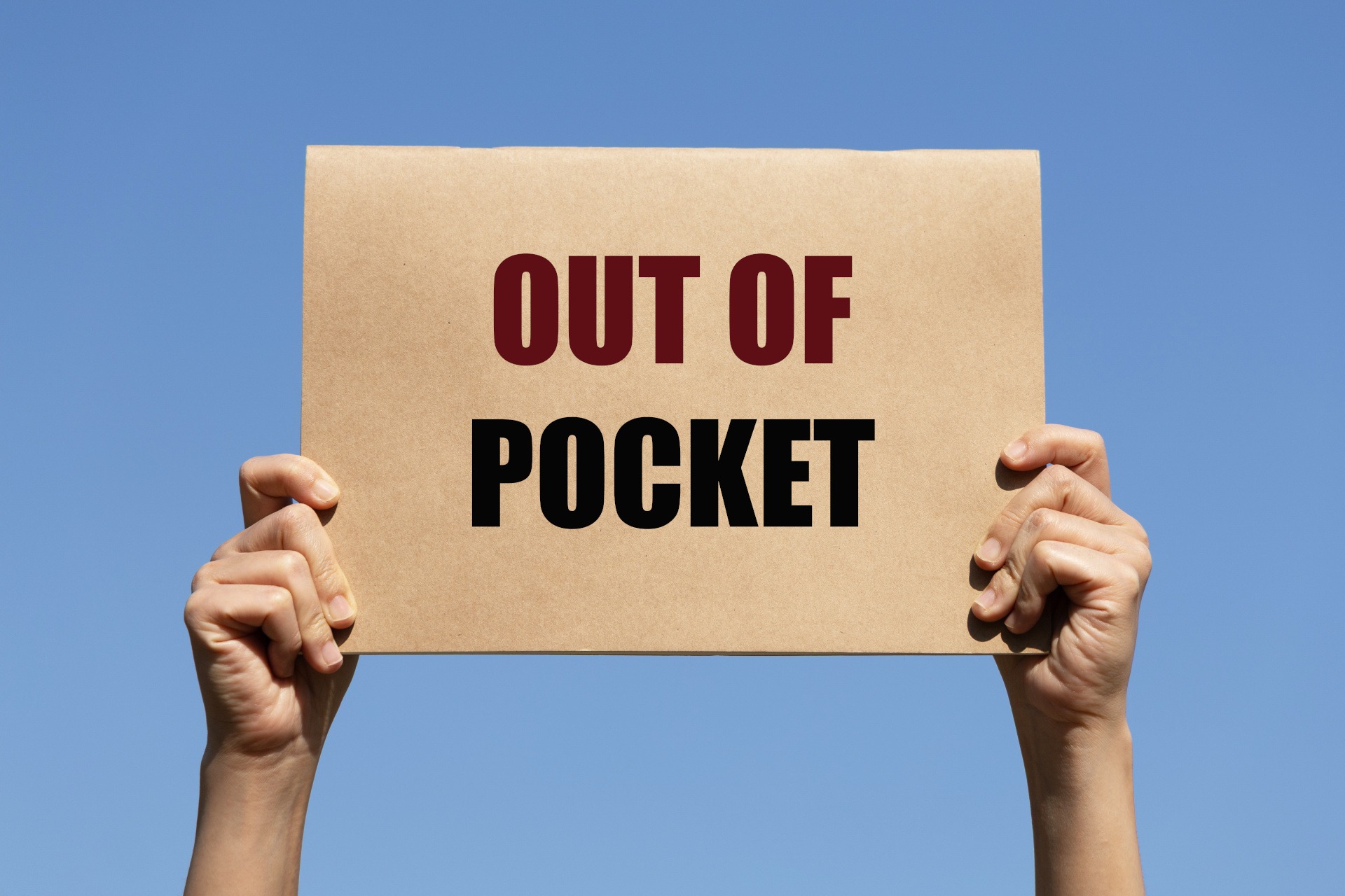 Hands holding a sign that reads "OUT OF POCKET" against a clear blue sky, highlighting the theme of Medicare out-of-pocket expenses.