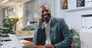 Smiling man in a business suit sitting at a desk with a laptop, representing personalized guidance in health insurance from Amerus Financial.