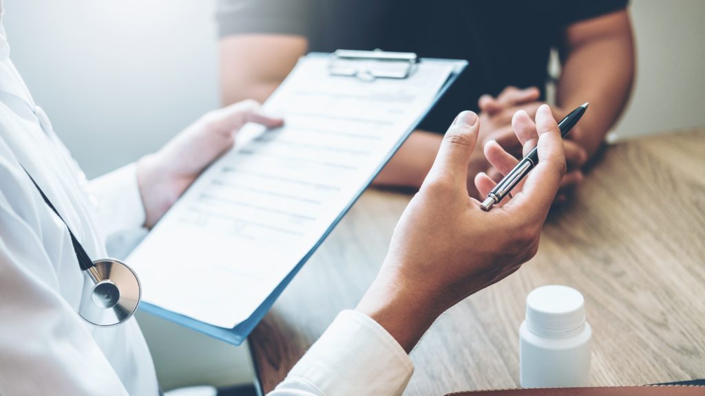 Doctor holding a clipboard and pen during a patient consultation about healthcare options and Medicare coverage.