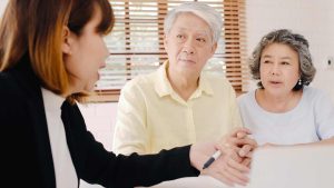Female insurance agent discussing Medicare options with elderly couple at a table, emphasizing personalized guidance and support for health insurance decisions.