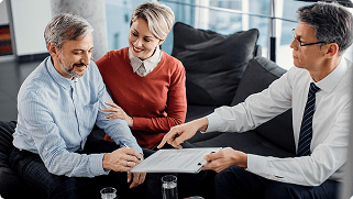 Couple discussing life insurance options with financial advisor, reviewing documents in modern office setting.