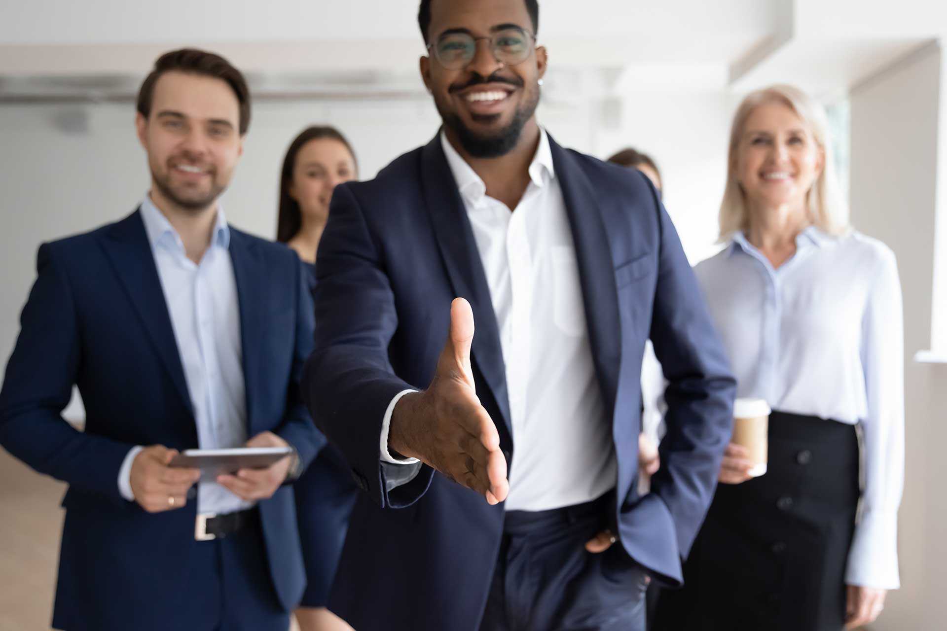 Group of professional insurance agents smiling and extending a handshake, showcasing personalized service and expertise at Amerus Financial.