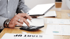 Person using a calculator and tablet while analyzing financial documents, emphasizing planning and decision-making in life insurance and financial strategies.