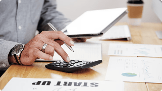 Person calculating retirement income using a calculator, tablet, and financial documents on a desk, emphasizing financial planning and tax advantages.