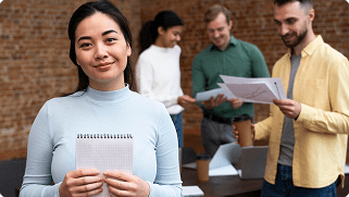 Woman holding a notepad in a collaborative business meeting, with colleagues reviewing documents and discussing group health insurance options.