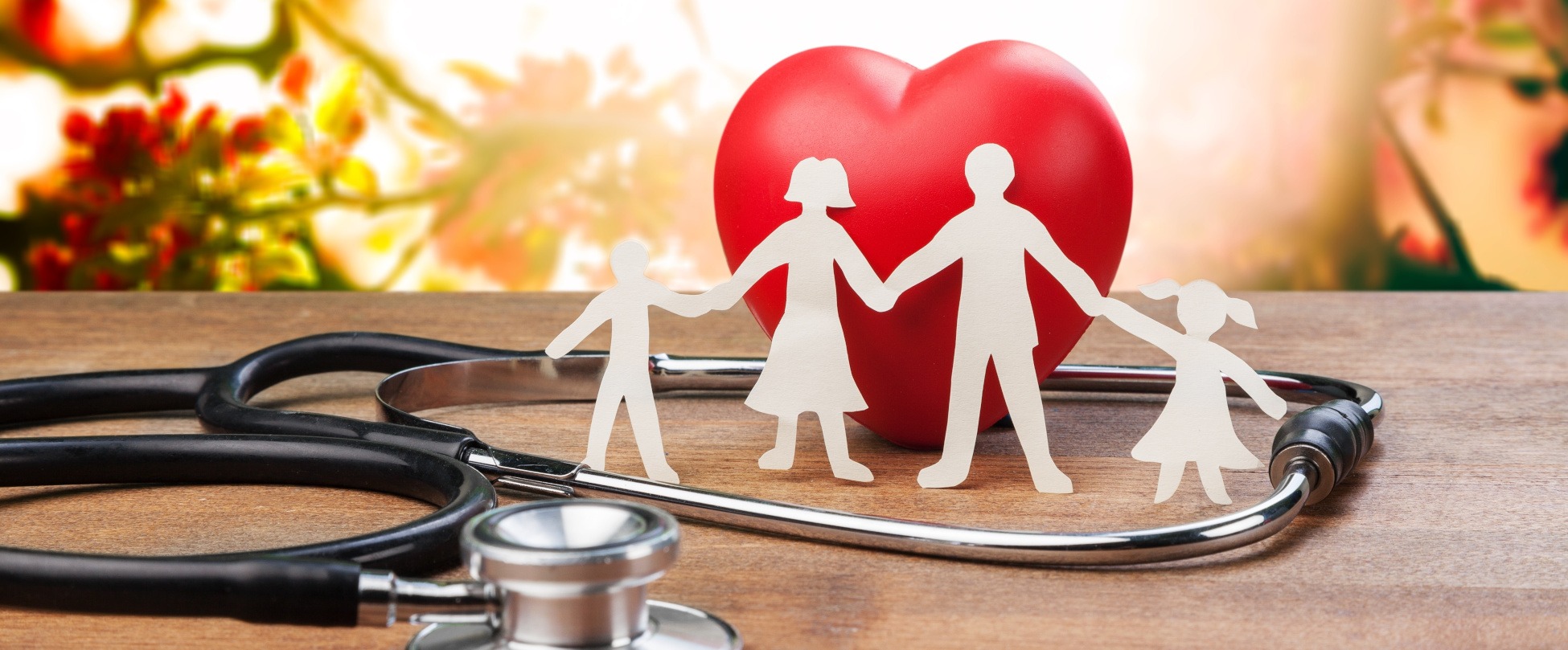 Paper cutouts of a family holding hands in front of a red heart and a stethoscope, symbolizing affordable health insurance for families.
