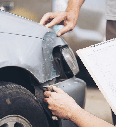 Person inspecting damaged car front with clipboard, relevant to Florida auto insurance claims and regulations.